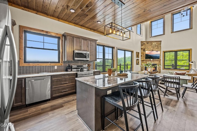 kitchen featuring a breakfast bar, appliances with stainless steel finishes, a kitchen island, dark brown cabinetry, and wood ceiling