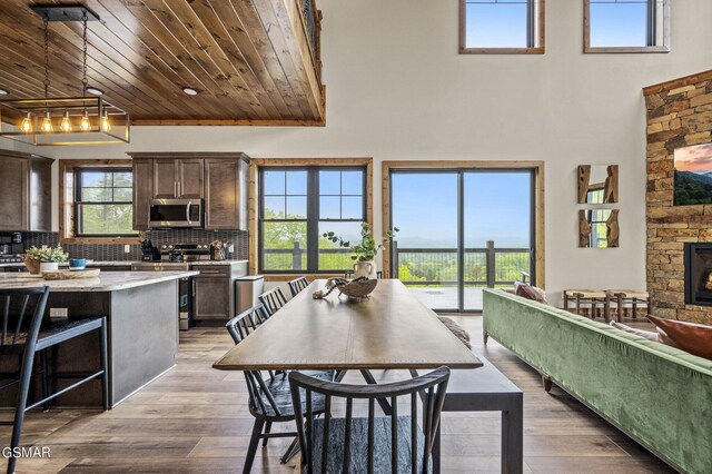 dining area featuring light wood-type flooring, wood ceiling, a fireplace, and a towering ceiling