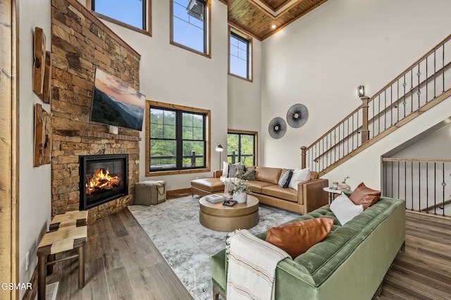 living room featuring a wealth of natural light, dark wood-type flooring, wooden ceiling, a high ceiling, and a stone fireplace