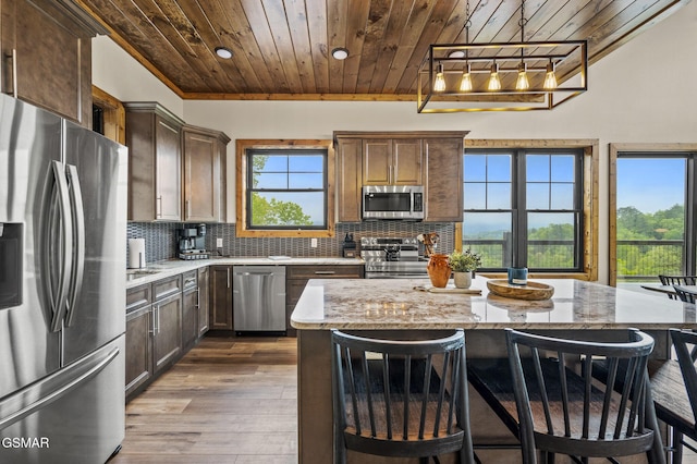 kitchen with decorative backsplash, appliances with stainless steel finishes, light stone counters, wood ceiling, and a center island