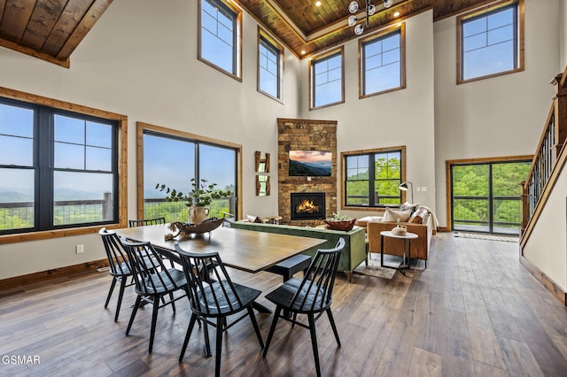 dining space with a high ceiling, a stone fireplace, wooden ceiling, and wood-type flooring