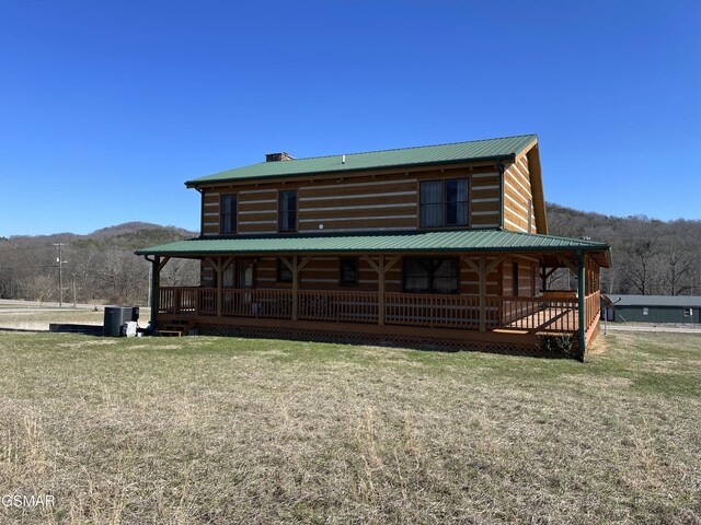 rear view of property with metal roof, central AC unit, a mountain view, covered porch, and a yard