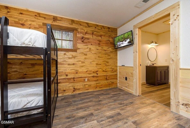 unfurnished bedroom featuring connected bathroom, sink, dark hardwood / wood-style floors, and wood walls