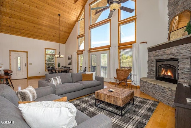 living room with a stone fireplace, ceiling fan with notable chandelier, hardwood / wood-style floors, high vaulted ceiling, and wooden ceiling