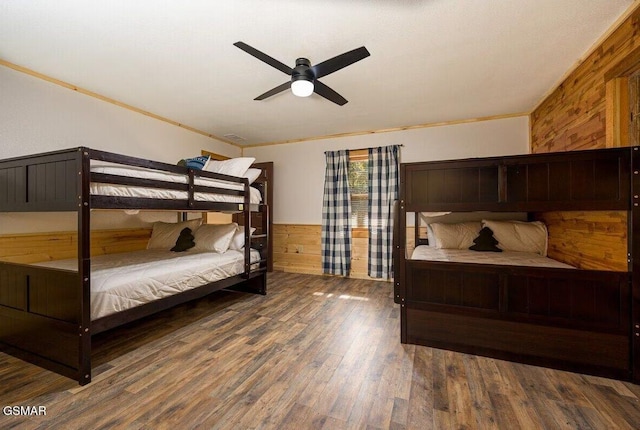 bedroom featuring wooden walls, ornamental molding, dark hardwood / wood-style floors, and ceiling fan