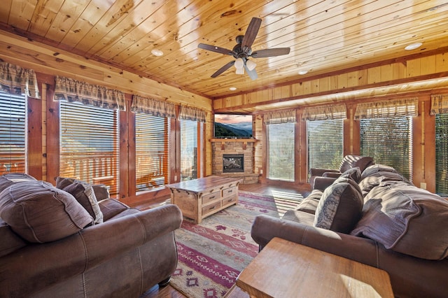 living room with ceiling fan, wood walls, a stone fireplace, and wooden ceiling