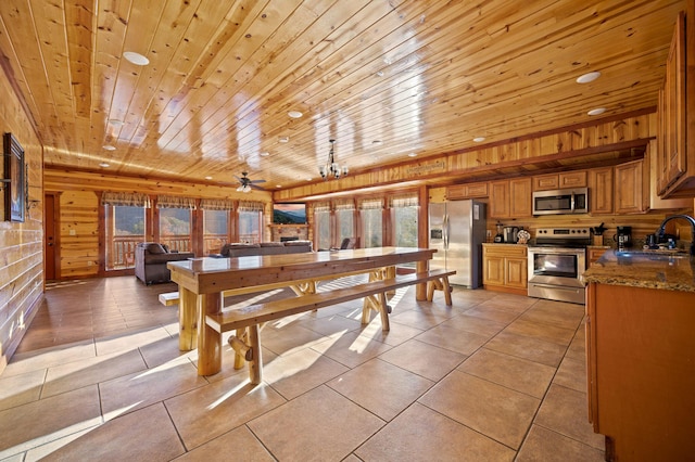 dining room with wood ceiling, ceiling fan with notable chandelier, wooden walls, sink, and light tile patterned floors