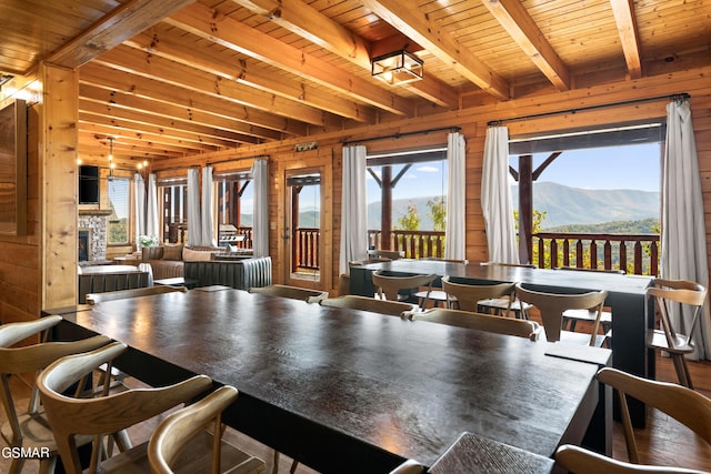 dining room featuring beamed ceiling, a stone fireplace, wood ceiling, a mountain view, and wood walls