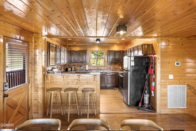 kitchen featuring kitchen peninsula, stainless steel fridge, light wood-type flooring, wooden ceiling, and wooden walls