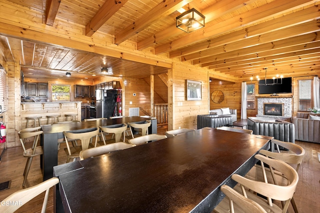 dining area with wood-type flooring, a fireplace, wooden ceiling, wood walls, and beamed ceiling