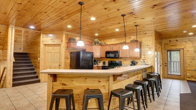 kitchen with wooden walls, light tile patterned floors, black appliances, and decorative light fixtures