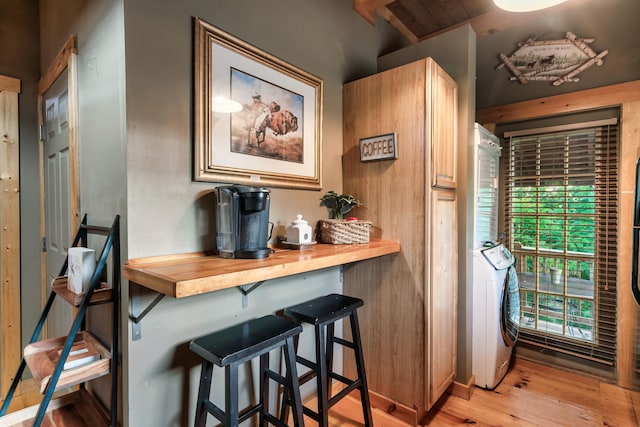 bar featuring washer / dryer, light wood-type flooring, and wooden counters