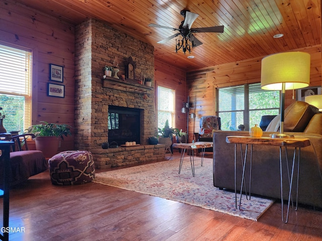 living room featuring ceiling fan, wooden ceiling, a stone fireplace, wood walls, and hardwood / wood-style flooring