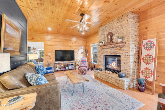 living room featuring a stone fireplace, wood walls, wood-type flooring, ceiling fan, and wood ceiling