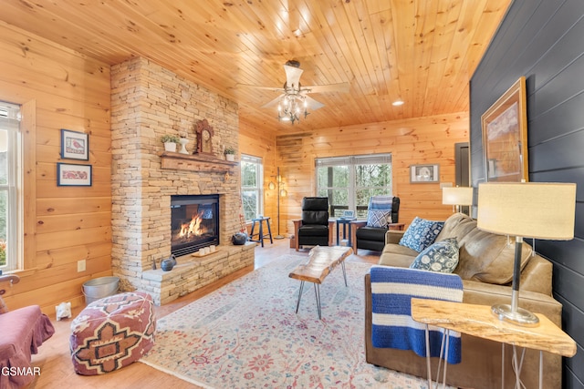 living room featuring a stone fireplace, hardwood / wood-style floors, wooden walls, ceiling fan, and wooden ceiling