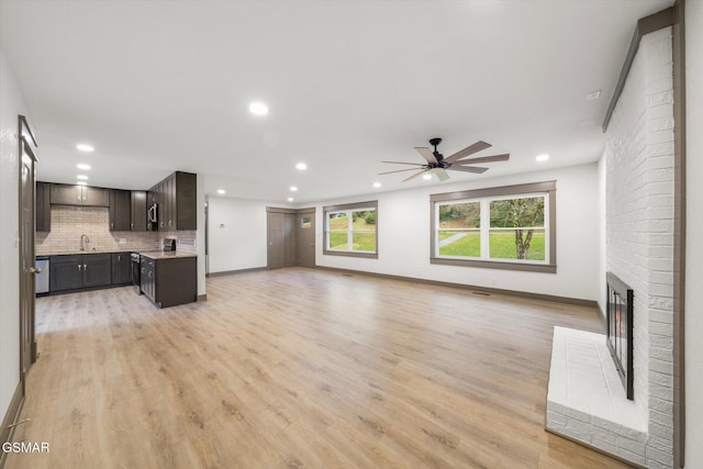 unfurnished living room with light wood-style floors, a fireplace, a sink, and recessed lighting