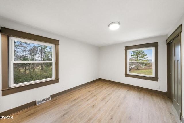 unfurnished room featuring light wood finished floors, plenty of natural light, visible vents, and baseboards