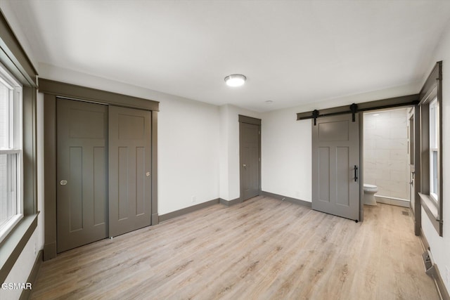 unfurnished bedroom with multiple closets, a barn door, light wood-type flooring, and baseboards