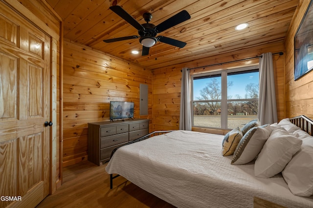 bedroom with ceiling fan, wood ceiling, wood walls, and light hardwood / wood-style floors