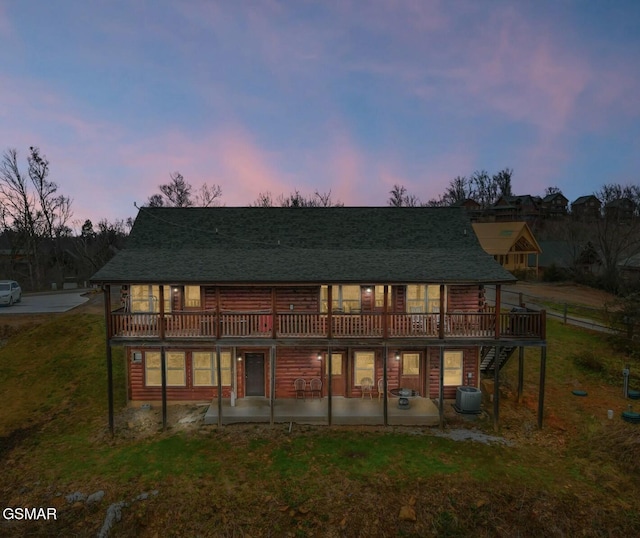 back house at dusk with central AC, a wooden deck, a yard, and a patio