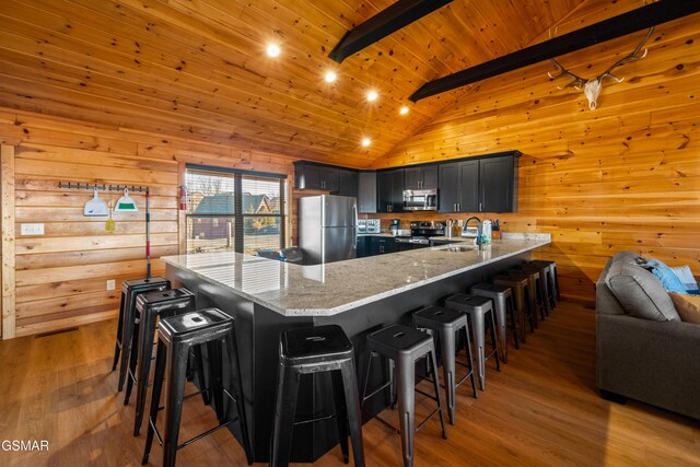 kitchen featuring a kitchen bar, appliances with stainless steel finishes, beamed ceiling, and wooden ceiling