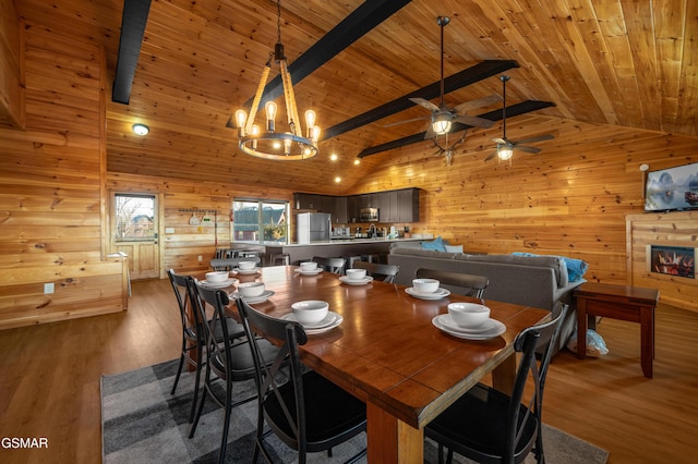 dining room with wood walls, wood-type flooring, lofted ceiling with beams, ceiling fan with notable chandelier, and wooden ceiling