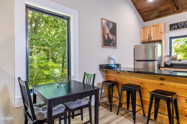 dining room featuring a healthy amount of sunlight, light hardwood / wood-style flooring, lofted ceiling, and wood ceiling