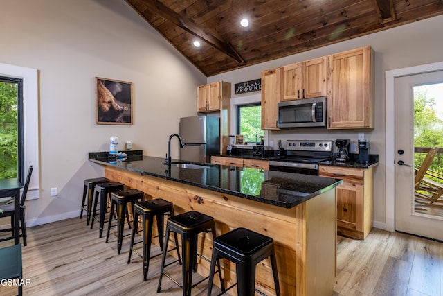 kitchen featuring stainless steel appliances, lofted ceiling with beams, kitchen peninsula, dark stone countertops, and a breakfast bar