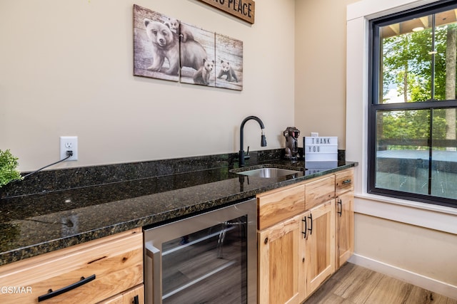 kitchen with light brown cabinets, dark stone counters, sink, light hardwood / wood-style flooring, and beverage cooler