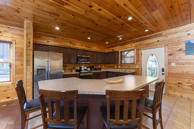 kitchen with dark brown cabinetry, wood walls, light tile patterned flooring, wood ceiling, and appliances with stainless steel finishes