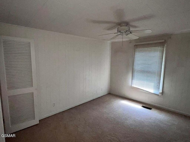 spare room featuring ceiling fan, wooden walls, and carpet floors