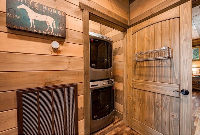 clothes washing area with hardwood / wood-style floors, wood walls, and stacked washer / dryer