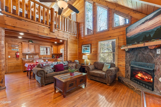 living area featuring wooden ceiling, wood walls, light wood finished floors, and a stone fireplace