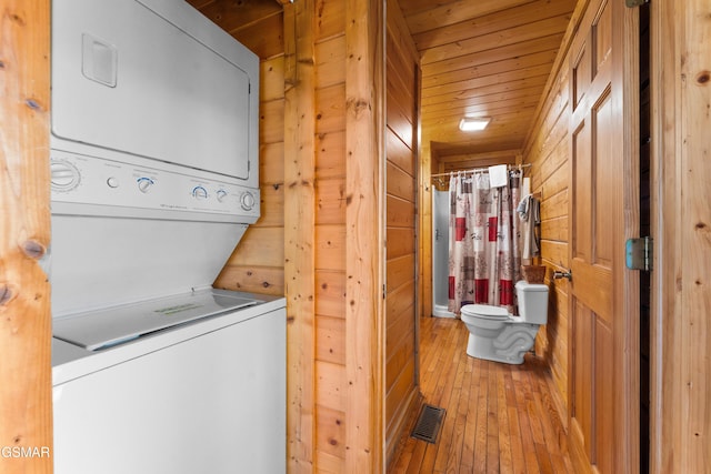 clothes washing area with wooden walls, visible vents, wood ceiling, stacked washing maching and dryer, and hardwood / wood-style floors