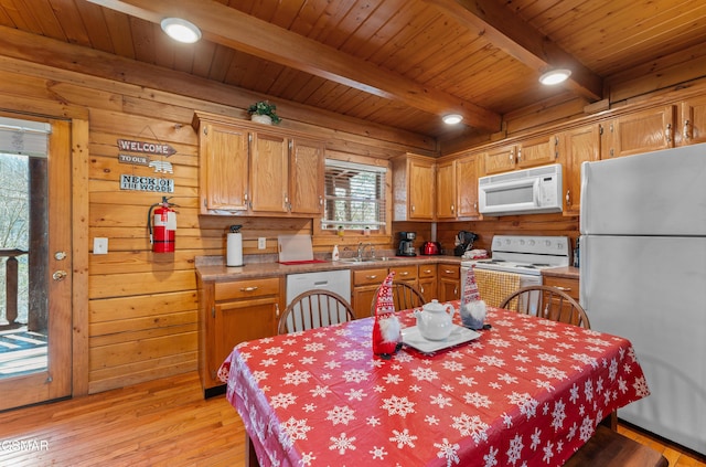 kitchen with white appliances, wooden walls, a sink, light wood-style floors, and beam ceiling