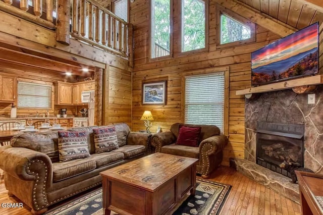 living room with light hardwood / wood-style floors, a towering ceiling, wooden walls, a stone fireplace, and wooden ceiling