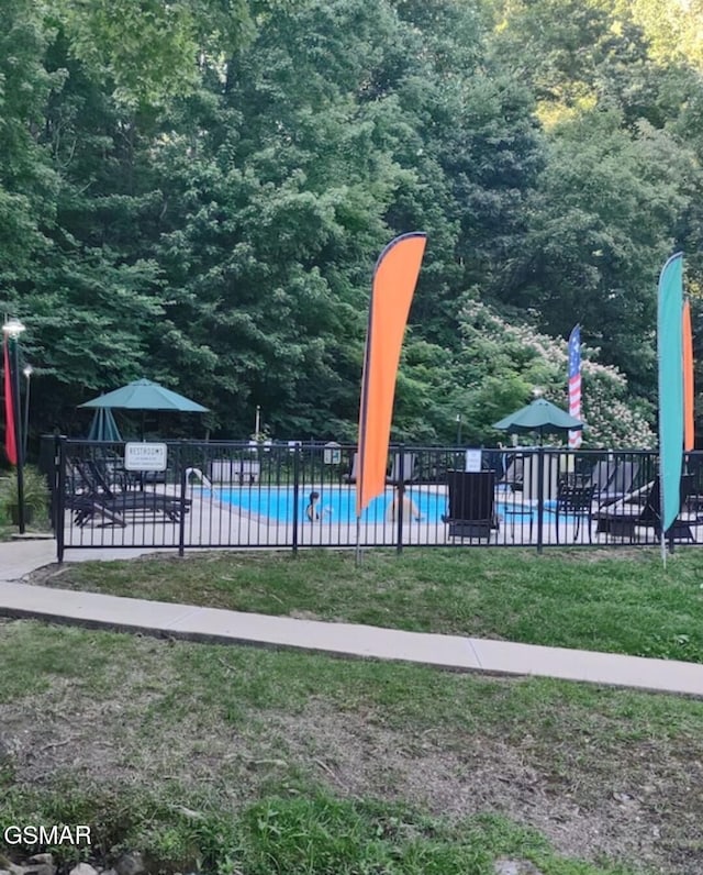 view of jungle gym with a yard, a forest view, fence, and a community pool