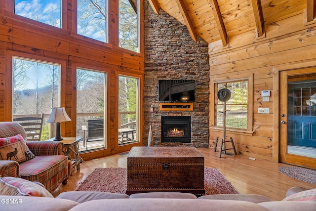 living room with lofted ceiling with beams, wood ceiling, wood finished floors, a stone fireplace, and wood walls