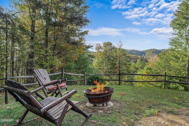 view of yard with fence, a fire pit, and a wooded view