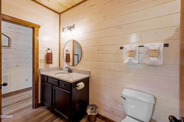 bathroom featuring vanity, hardwood / wood-style floors, wooden walls, and toilet