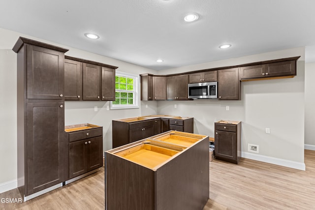 kitchen with stainless steel microwave, dark brown cabinets, light wood-type flooring, baseboards, and recessed lighting