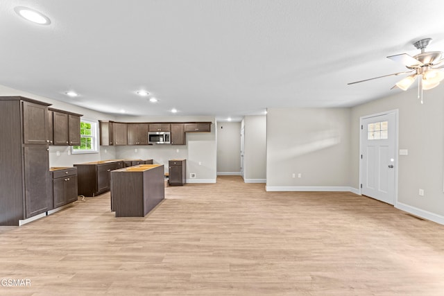 kitchen featuring stainless steel microwave, a kitchen island, dark brown cabinetry, ceiling fan, and light wood-style flooring