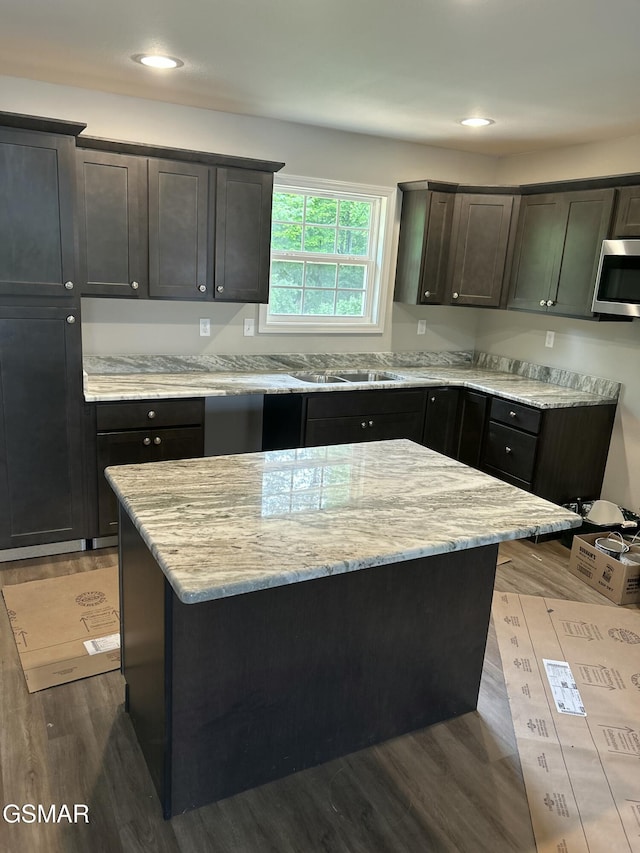 kitchen with stainless steel microwave, wood finished floors, light stone counters, a sink, and recessed lighting