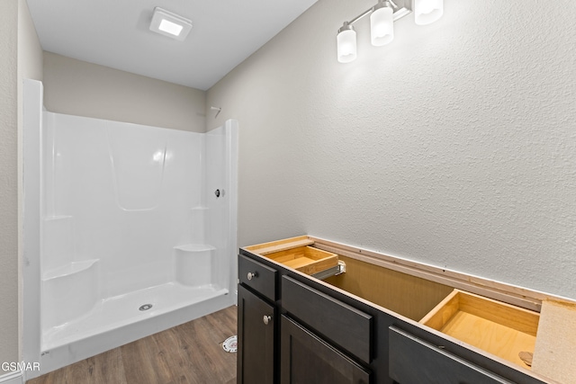full bathroom featuring wood finished floors, a shower, and a textured wall