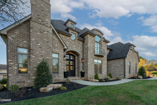 view of front of house with a balcony, a front yard, and french doors