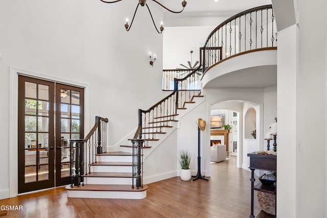 stairs with french doors, ornamental molding, hardwood / wood-style floors, a notable chandelier, and a high ceiling