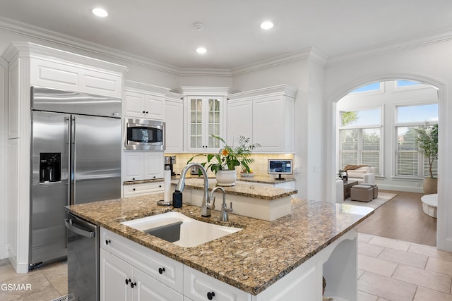 kitchen with built in appliances, white cabinets, sink, and a kitchen island with sink