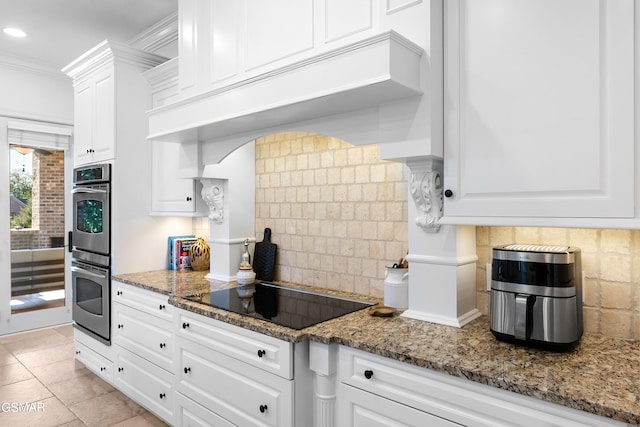 kitchen featuring backsplash, black electric stovetop, dark stone countertops, stainless steel double oven, and white cabinetry