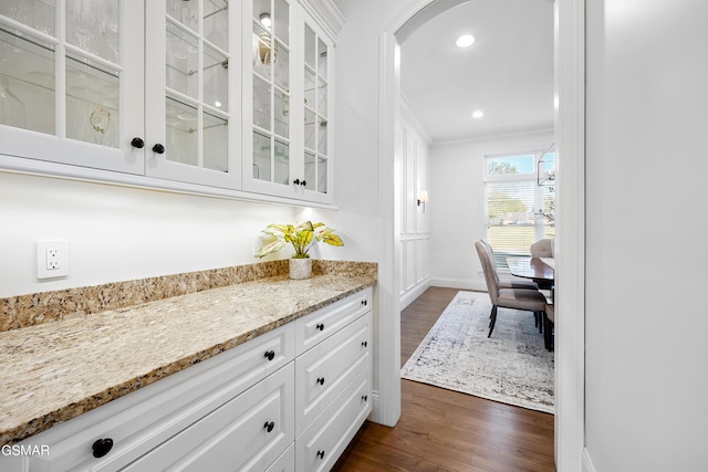 interior space featuring white cabinets, dark hardwood / wood-style floors, light stone counters, and ornamental molding