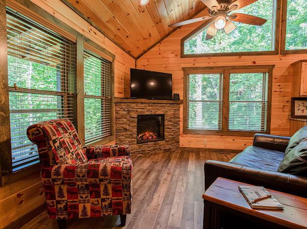 living room featuring wood ceiling, vaulted ceiling, hardwood / wood-style floors, a stone fireplace, and wood walls